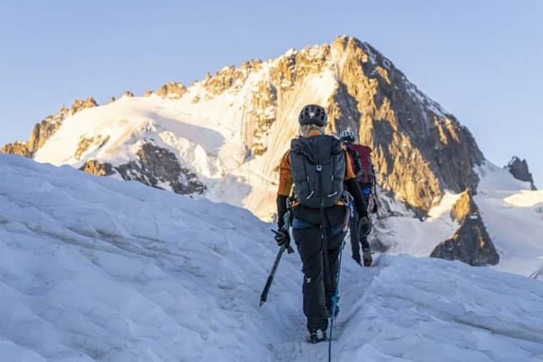 Cordée d’alpinistes progressant sur un glacier enneigé au lever du soleil, au pied d’un sommet alpin illuminé par une lumière dorée.