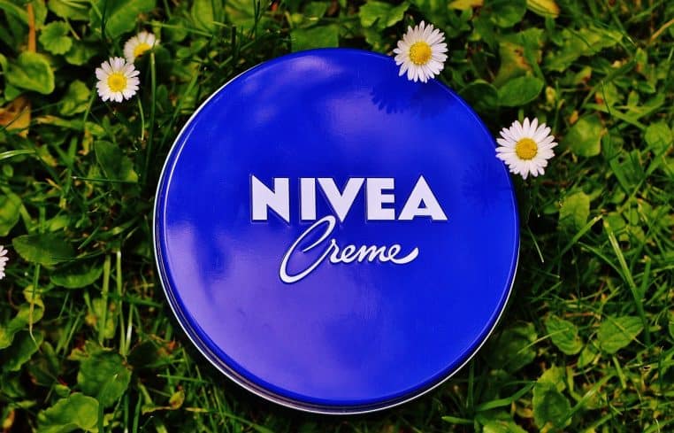 Gros plan sur un pot bleu de crème Nivea ouvert, posé sur une surface claire, prêt à être appliqué sur la peau du visage.
