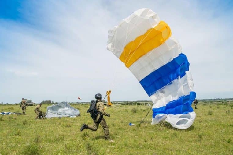 Militaires équipés de parachutes colorés pliant et sécurisant leur voile sur un champ, après un exercice de saut en groupe.