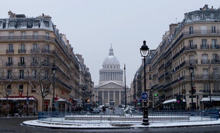 Immeubles haussmanniens à Paris bordant une rue enneigée, voitures et trottoirs recouverts de neige fraîche par temps froid