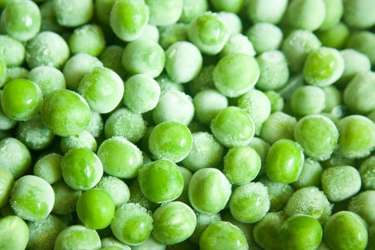 Gros plan sur des petits pois surgelés recouverts de givre, mettant en avant des légumes verts prêts à être cuisinés en quelques minutes.