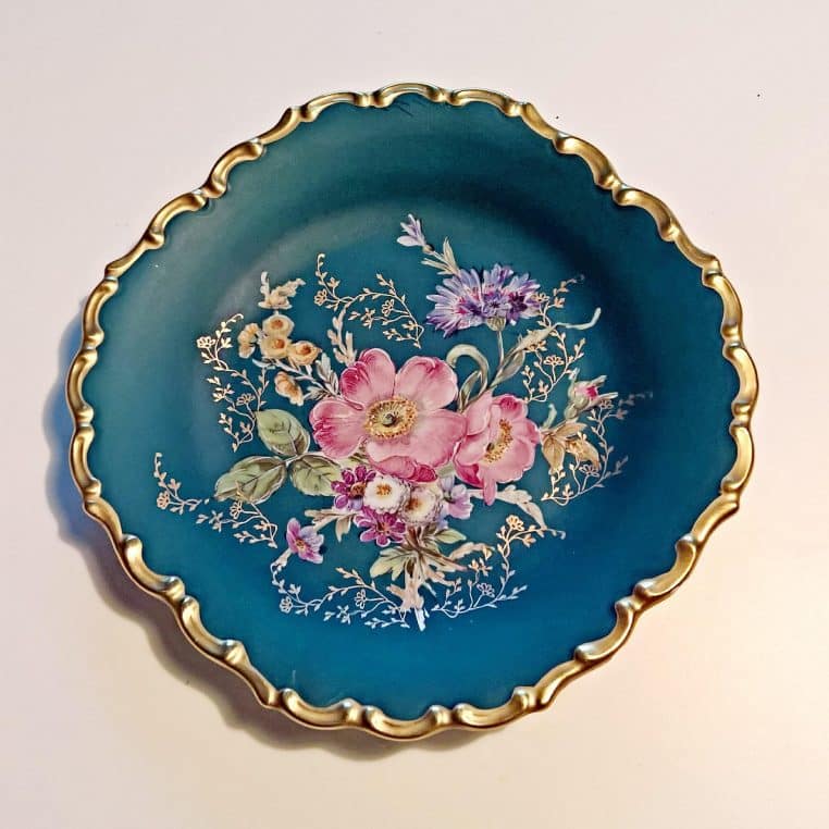 Assiette en porcelaine verte décorée de fleurs avec bord doré, photographiée de près comme une pièce de collection posée à plat.