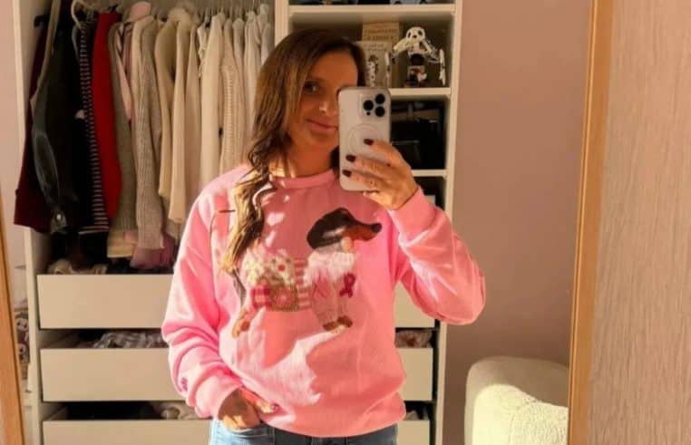 Selfie miroir de Sue Radford portant un pull rose à motif dachshund et ruban rose, devant un dressing baigné de soleil.