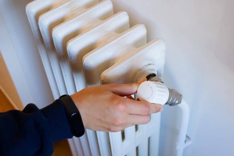 Gros plan sur une main réglant un thermostat de radiateur, symbole du contrôle précis de la température dans une pièce chauffée.