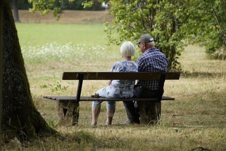 Deux retraités assis sur un banc dans un parc, discutant face à un paysage de campagne symbolisant la retraite à l’étranger