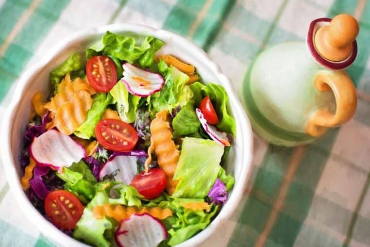 Bol de salade croquante avec feuilles de laitue, tomates cerises et rondelles de radis, accompagné d’une bouteille de sauce.