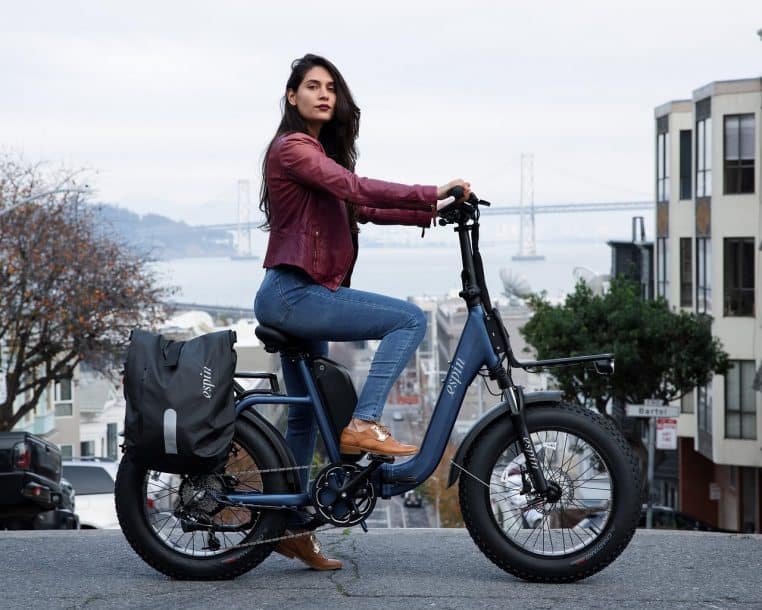 Femme à vélo électrique dans une rue de San Francisco, entourée de voitures, illustrant la cohabitation délicate entre cyclistes et trafic motorisé en milieu urbain.