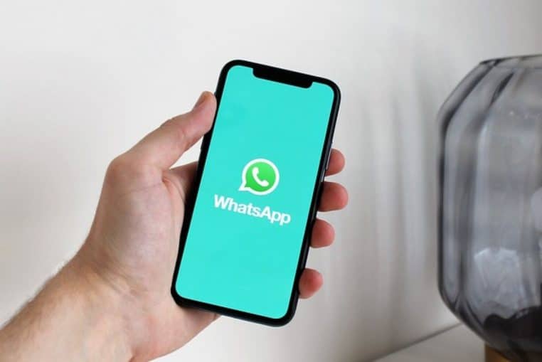 Main tenant un smartphone affichant l’écran d’accueil WhatsApp en plein écran, vue rapprochée.