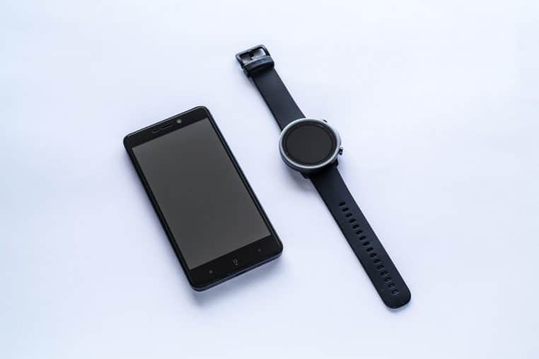 Smartphone posé à côté d’une montre connectée à écran noir sur une surface claire, symbolisant l’écosystème numérique au cœur de la vie quotidienne