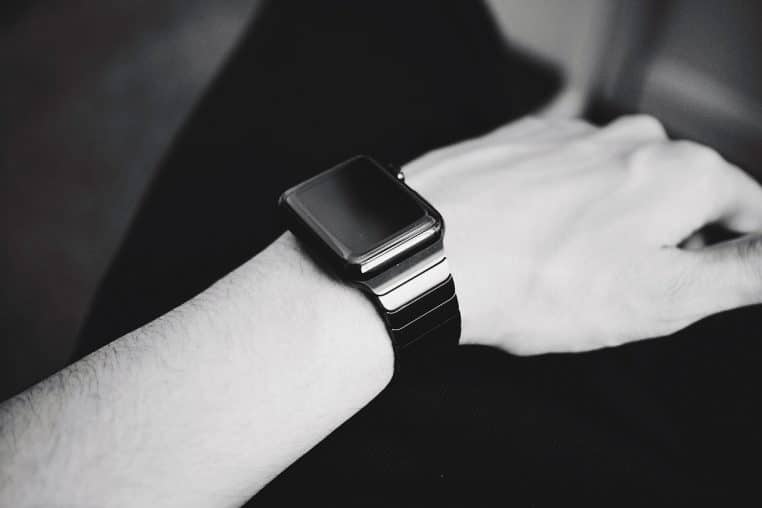 Montre connectée noire posée près d’un smartphone sur une table en bois claire, illustrant l’association entre téléphone et smartwatch au quotidien