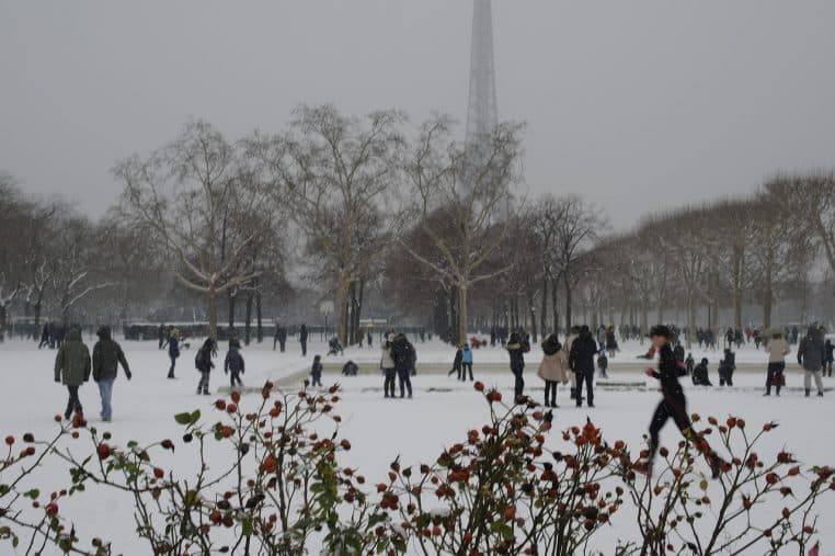 Vue enneigée du Champ-de-Mars à Paris avec la Tour Eiffel dans la brume et de nombreux promeneurs dans le parc.