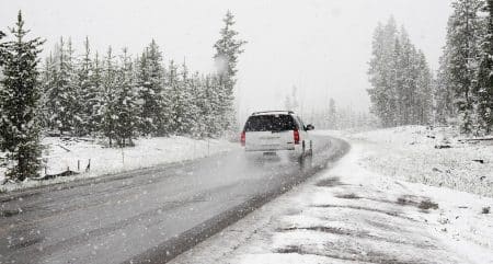 SUV blanc de dos circulant sur une route de montagne enneigée, sous une forte chute de neige, forêt de conifères en arrière-plan