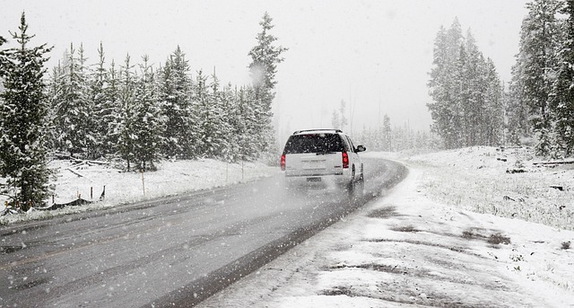 Voiture roulant sur une route partiellement enneigée sous une chute de neige dense, illustrant les risques de glissade sur chaussée froide