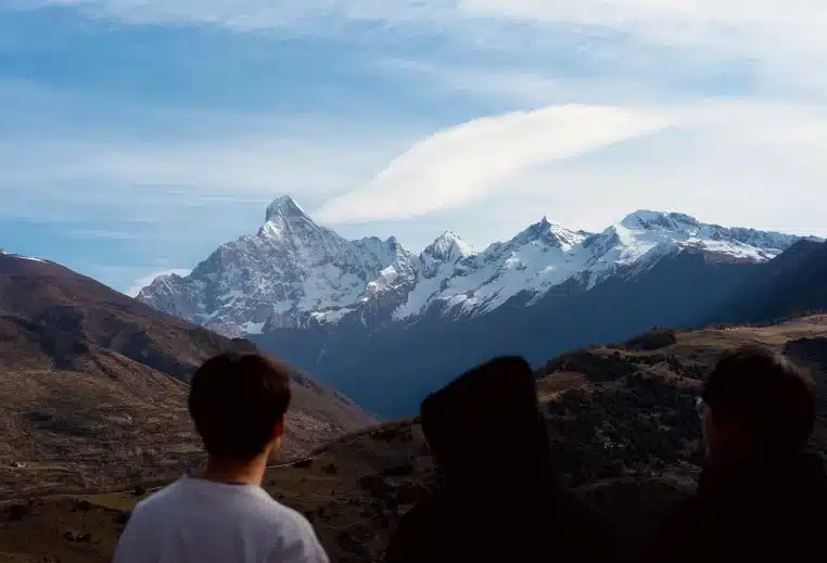Trois personnes de dos admirent une haute chaîne de montagnes enneigées sous un ciel dégagé, signe d’un temps froid mais lumineux en altitude