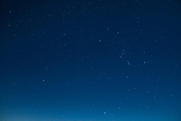 Ciel nocturne saturé d’étoiles en longue exposition, avec un léger relief sombre à l’horizon qui souligne l’immensité du cosmos.