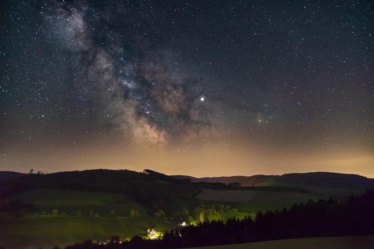 Voie lactée très nette dans un ciel nocturne profond, au-dessus d’un paysage de nature presque entièrement plongé dans l’obscurité.