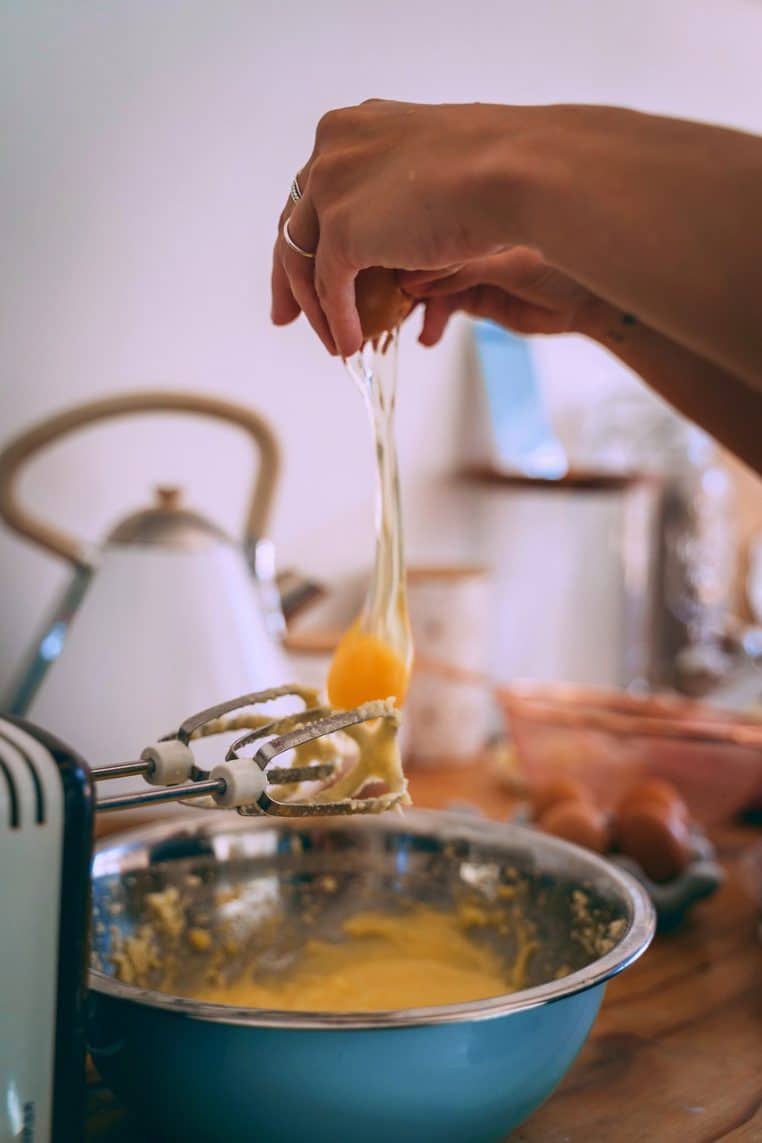 Gros plan sur un mixeur plongeant en action dans un saladier en verre rempli de pâte claire sur un plan de travail de cuisine.