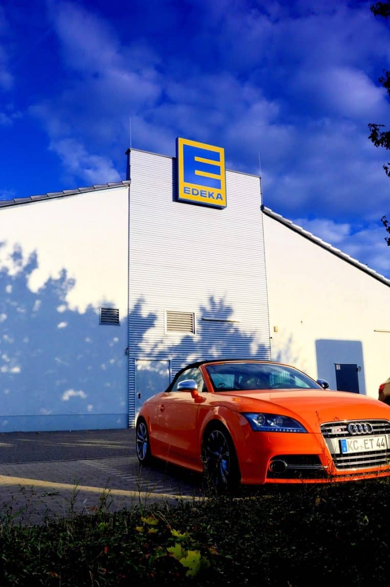 Voitures alignées sur un grand parking devant un supermarché moderne, prises en vue large en plein jour.