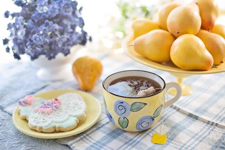 Tasse de thé fumant posée près de biscuits secs sur une table sombre, rappelant la différence entre boisson chaude non sucrée et en-cas sucré à limiter.