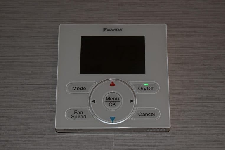 Commande murale de chauffage et climatisation avec écran numérique, installée dans une chambre d’hôtel moderne et bien chauffée.