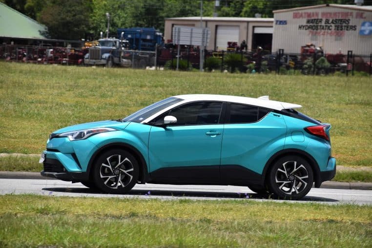 Toyota C-HR turquoise photographiée de profil en mouvement sur une route urbaine, soulignant son design de SUV coupé compact.