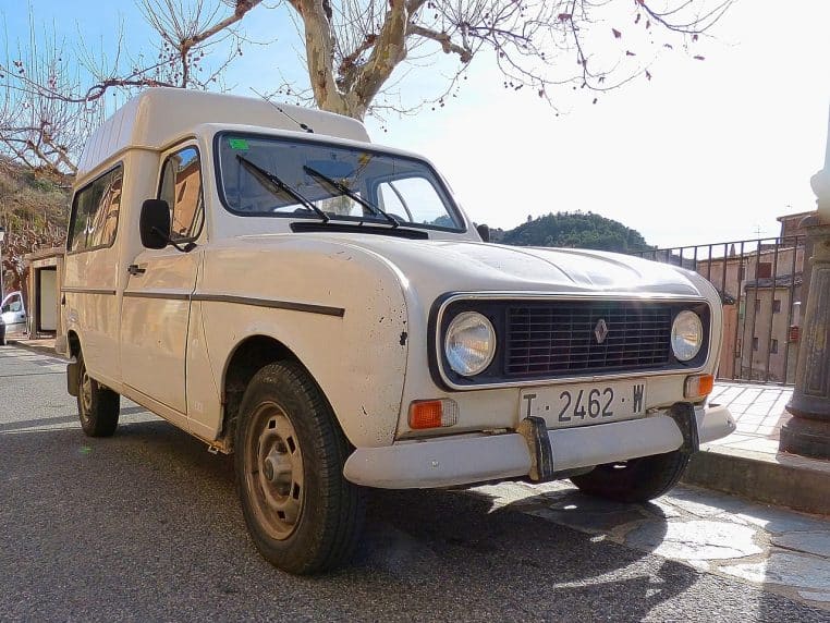 Fourgonnette Renault 4L blanche en version utilitaire, stationnée dans un village ensoleillé, montrant l’aspect polyvalent du modèle.