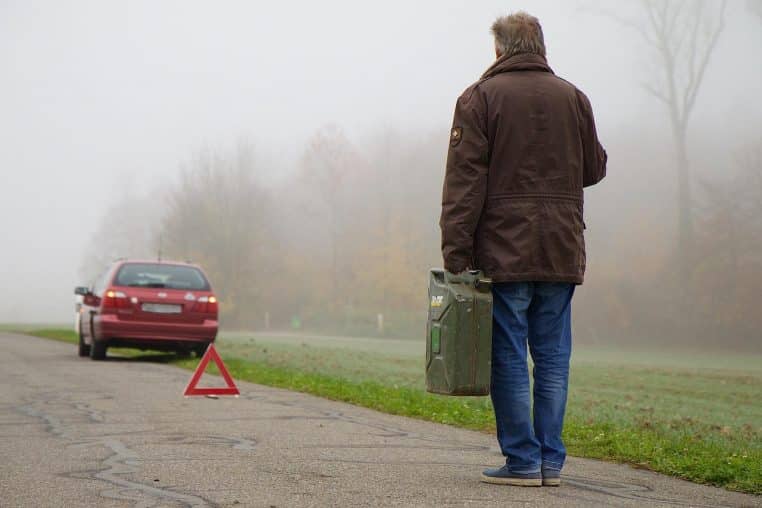 Conducteur marchant sur le bas-côté dans le brouillard vers sa voiture en panne, avec un triangle de présignalisation déjà déployé sur la route