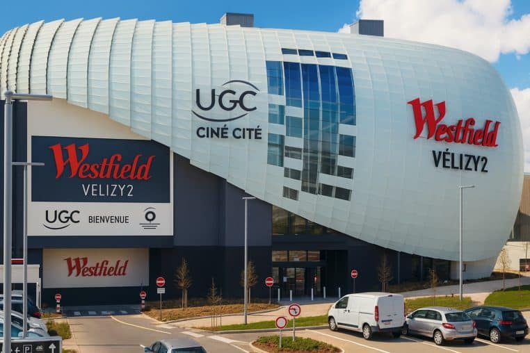 Façade contemporaine du centre commercial Westfield Vélizy 2 avec la coque blanche arrondie, les logos Westfield et UGC Ciné Cité bien visibles et un parking de voitures au premier plan, sous un ciel bleu.