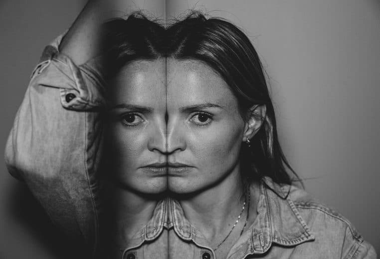 Portrait en noir et blanc d’une jeune femme face à un miroir, dont le reflet se superpose à son visage, symbolisant le regard complexe porté sur son propre corps.