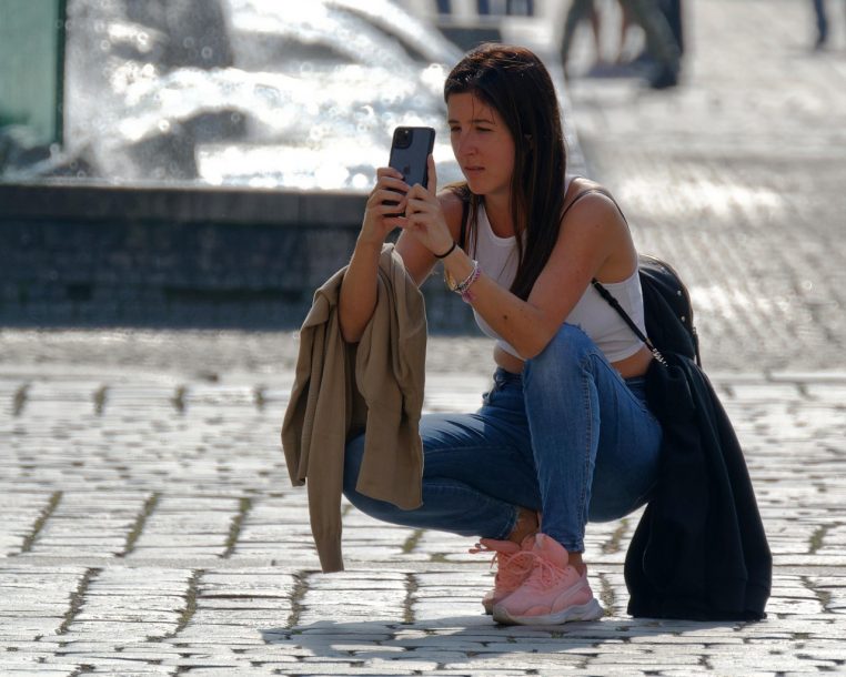 Femme assise dans un décor urbain, concentrée sur son smartphone, illustrant l’usage quotidien d’un forfait mobile en ville.