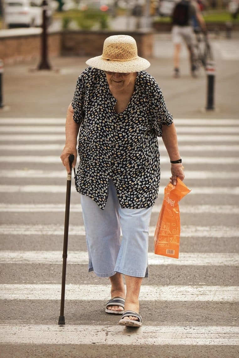 Femme âgée traversant une rue en ville avec un sac de courses, illustrant l’impact des décisions budgétaires sur le pouvoir d’achat des retraités.