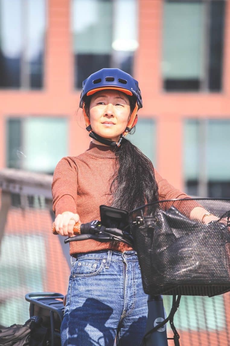 Cycliste urbaine casquée au guidon d’un vélo électrique roulant en ville, illustrant une utilisation responsable et équipée face aux dangers de la circulation dense.