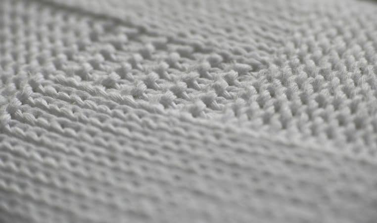 Gros plan d’un cardigan en maille blanche, motif tricoté apparent, illustrant une texture douce en laine et cachemire.