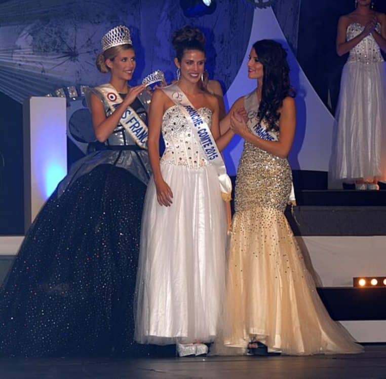Trois jeunes femmes en robes de soirée et couronnes posent côte à côte sur la scène de Miss Franche-Comté 2015, juste après l’annonce des résultats.