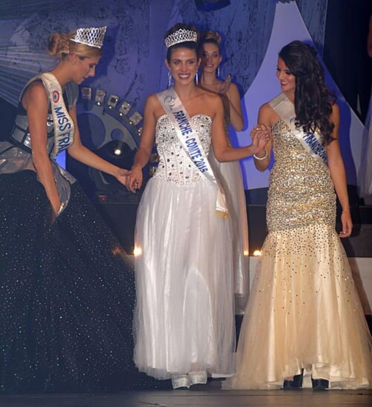 La nouvelle Miss Franche-Comté 2015 défile au centre de la scène, couronnée et en robe blanche, entourée de deux dauphines en robes dorées scintillantes.