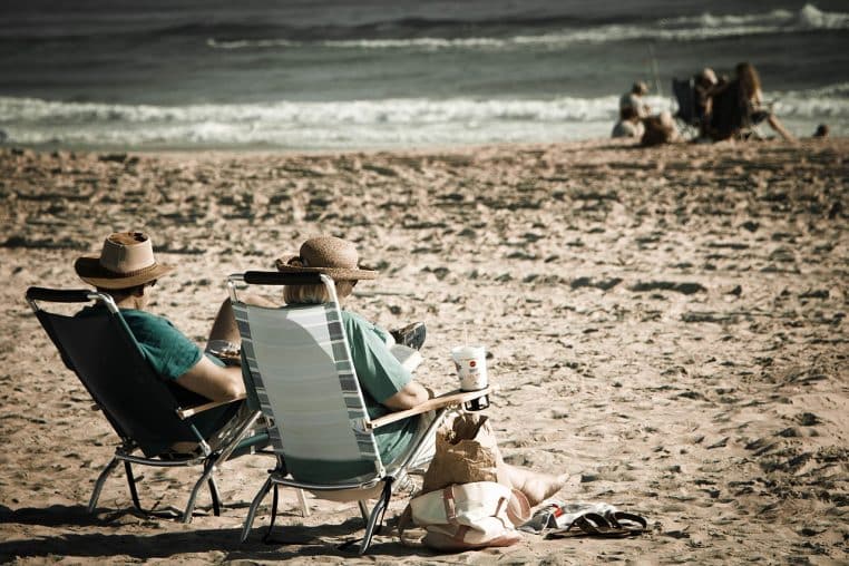 Couple âgé assis sur une plage, tourné vers la mer, profitant d’un moment de détente silencieux côte à côte