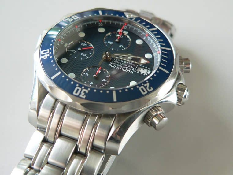 Gros plan d’une montre chronographe à lunette bleue, posée en biais, cadran et poussoirs visibles.