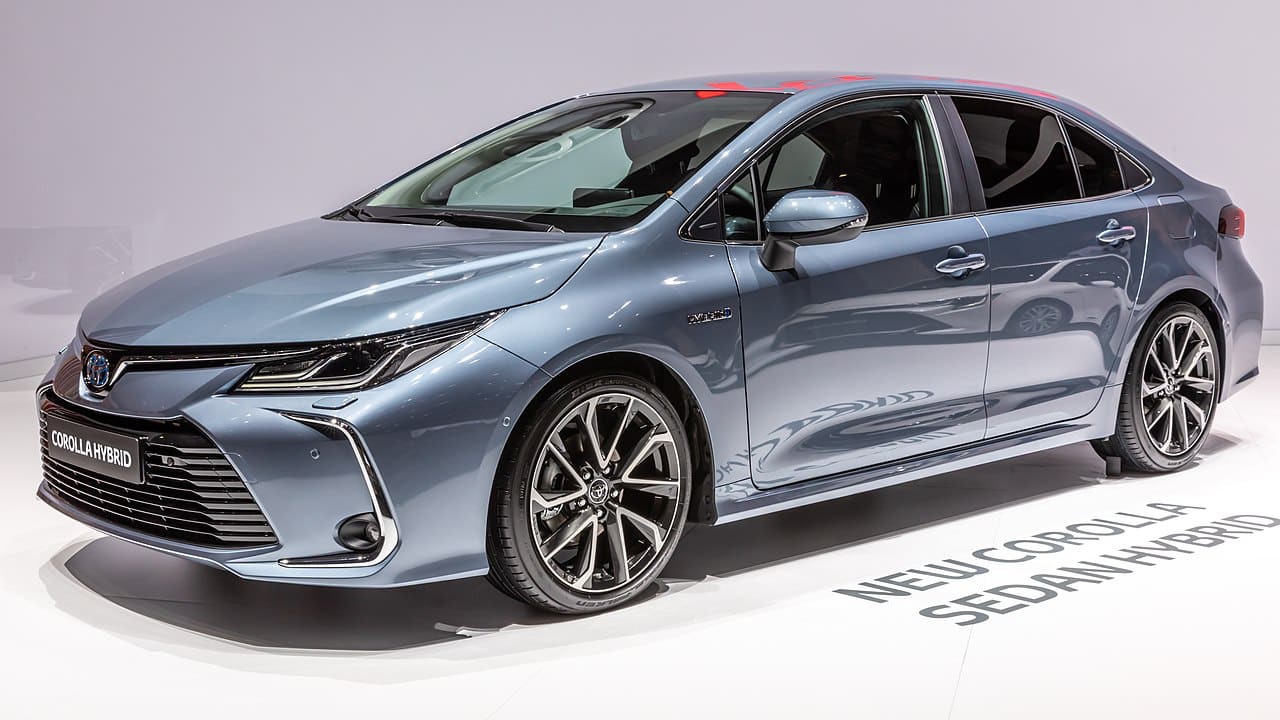 Toyota Corolla Hybrid berline grise exposée en intérieur sur podium, vue de trois quarts avant, éclairage de salon automobile.