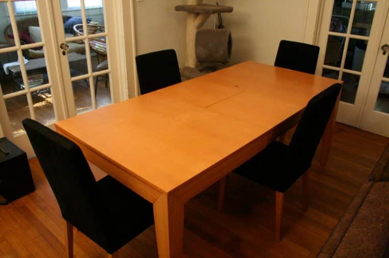 Table extensible en bois entièrement déployée dans une pièce lumineuse, plateau allongé prêt à recevoir.