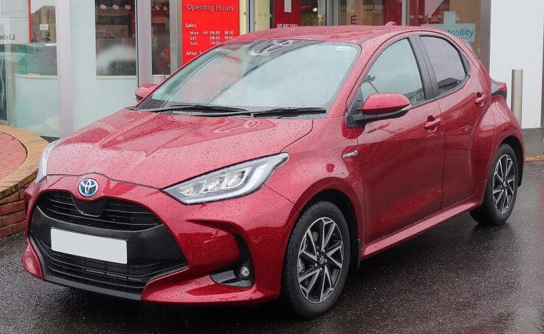 Toyota Yaris hybride rouge vue de trois quarts avant sur route mouillée, optiques LED et silhouette compacte.