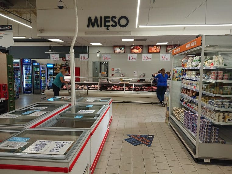 Rayon boucherie-traiteur d’un supermarché, employés en arrière-plan et vitrines réfrigérées au premier plan