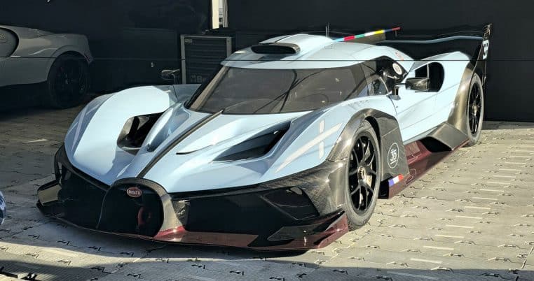 Bugatti Bolide 2024 noire et bleue en situation dynamique sur circuit, captée de trois-quarts avant avec fond de tribunes flou.