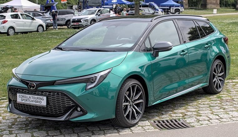 Toyota Corolla Touring Sports Hybrid vert métallisé, vue de trois quarts avant, stationnée sur un parking d’exposition en plein air.