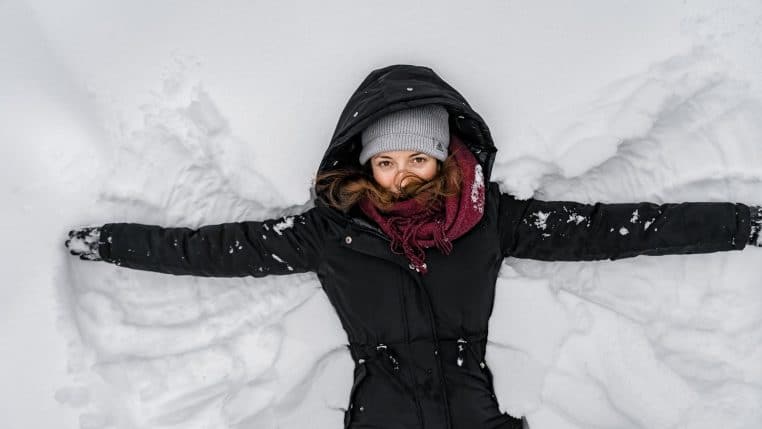 A woman in winter clothing making a snow angel, enjoying a snowy day outdoors.