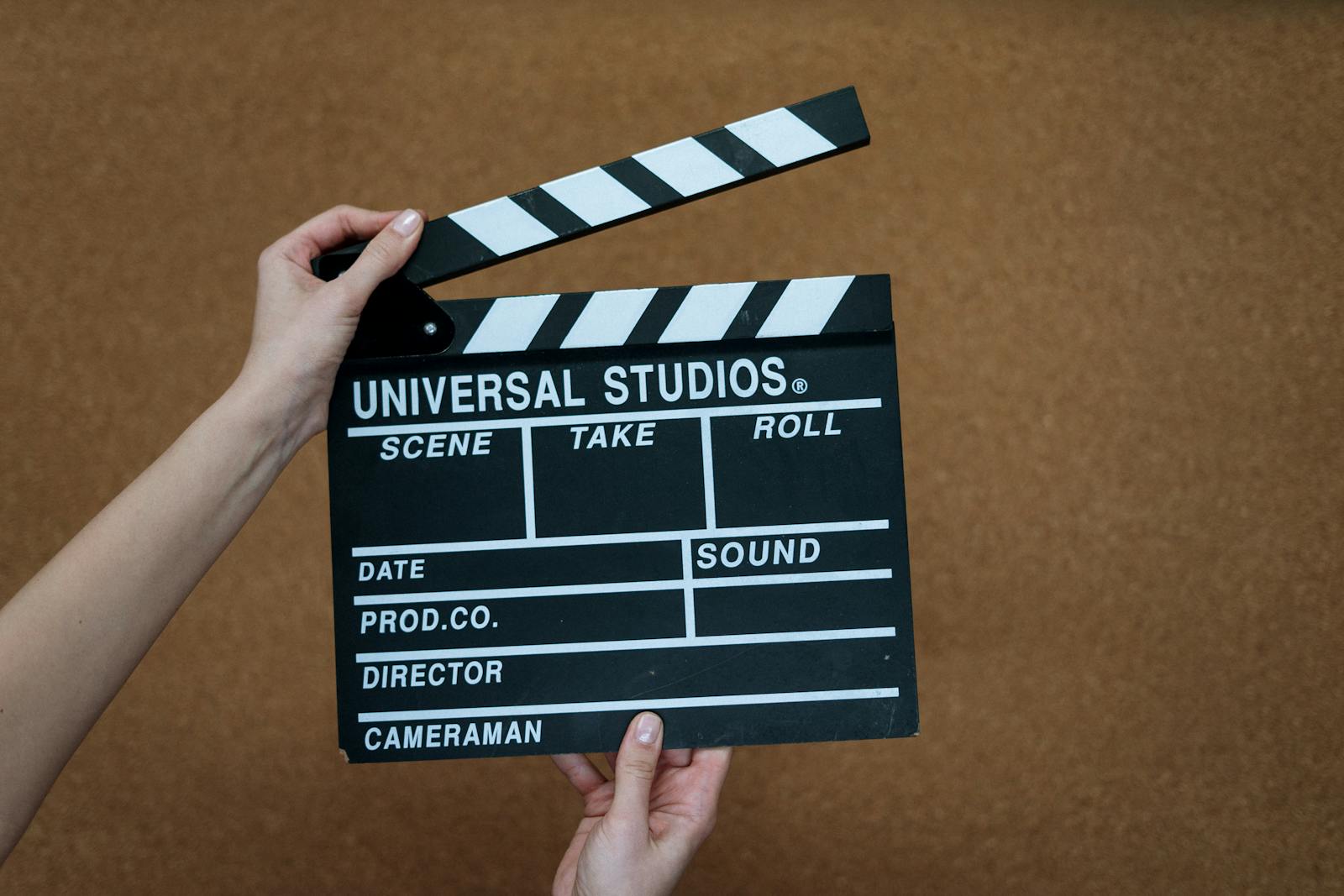 Close-up of hands holding a Universal Studios clapboard on a cork backdrop, ready for filming.