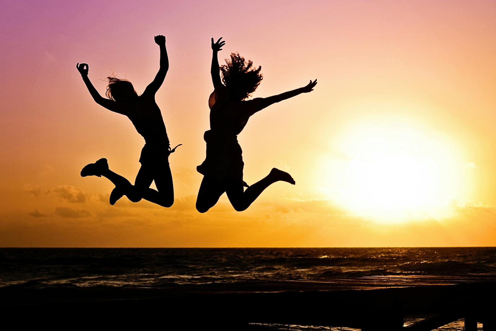 Silhouettes of two people joyfully jumping on a beach during a vibrant sunset.