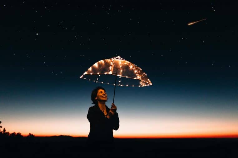 A joyful woman with a light-up umbrella stands under a starry sky, capturing a magical moment.