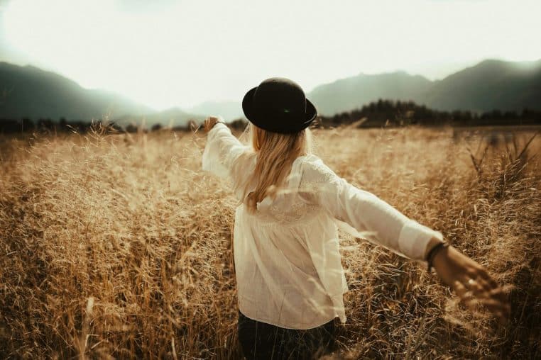 A woman in a field, arms outstretched, enjoying a peaceful autumn day.