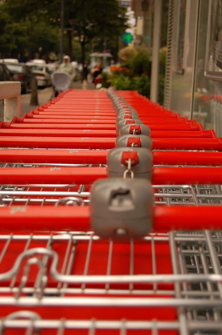 Alignement de chariots de supermarché métalliques prêts à l’entrée d’un magasin, symboles du passage en caisse.