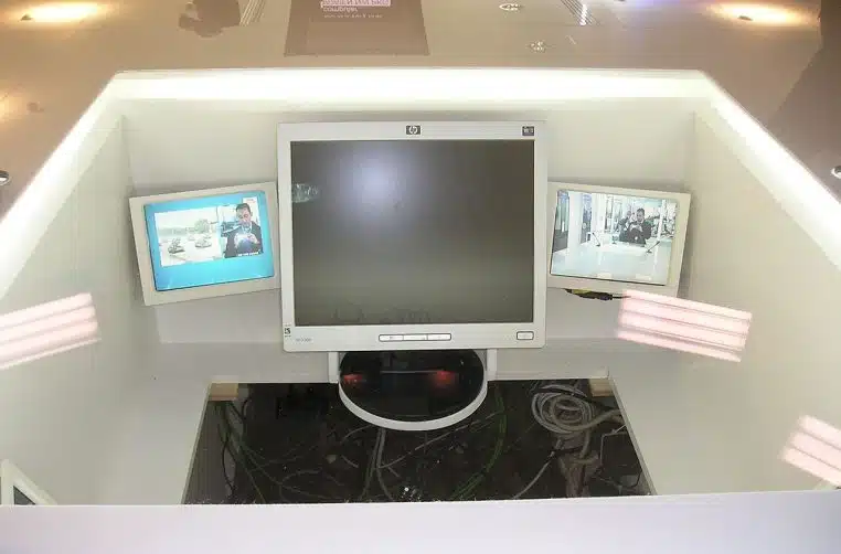 Vue d’un desk de studio TV avec écrans et matériel, ambiance plateau d’info en régie vitrée.